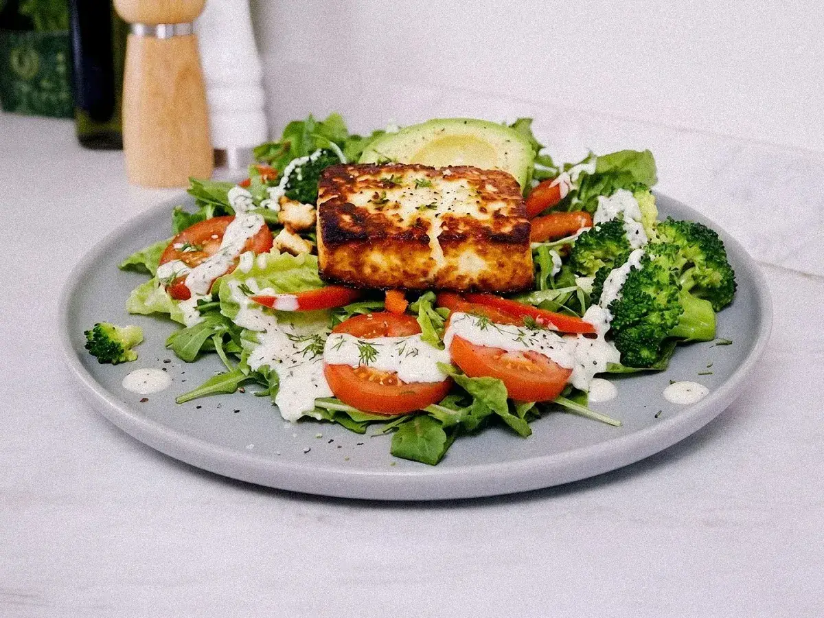 Gyllenstekt ost på en sallad med broccoli, tomat, avokado och en vit dressing